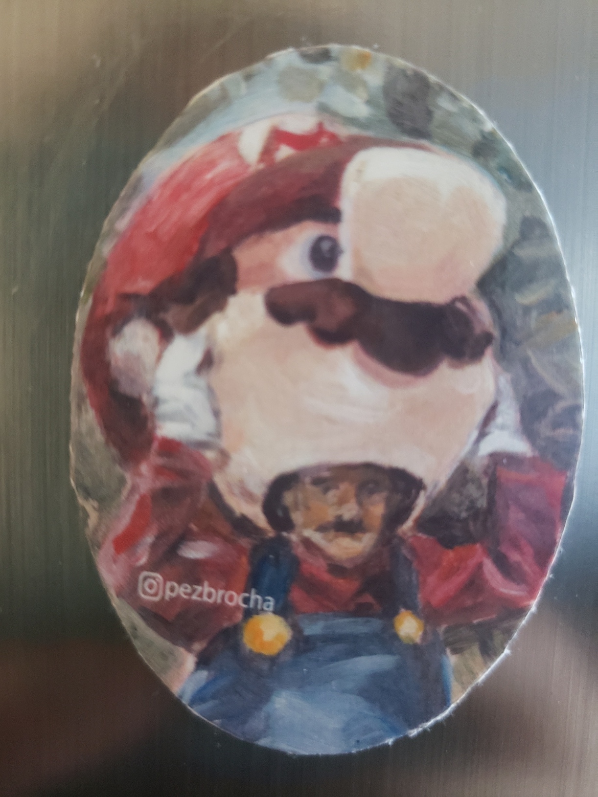 Imán de refrigerador. Tiene un print de una pintura acrílica del hombre que se parece a Mario Bros quitándose la cabeza de un disfraz de Mario Bros. Tiene una marca de agua referenciando a pezbrocha@instagram.com