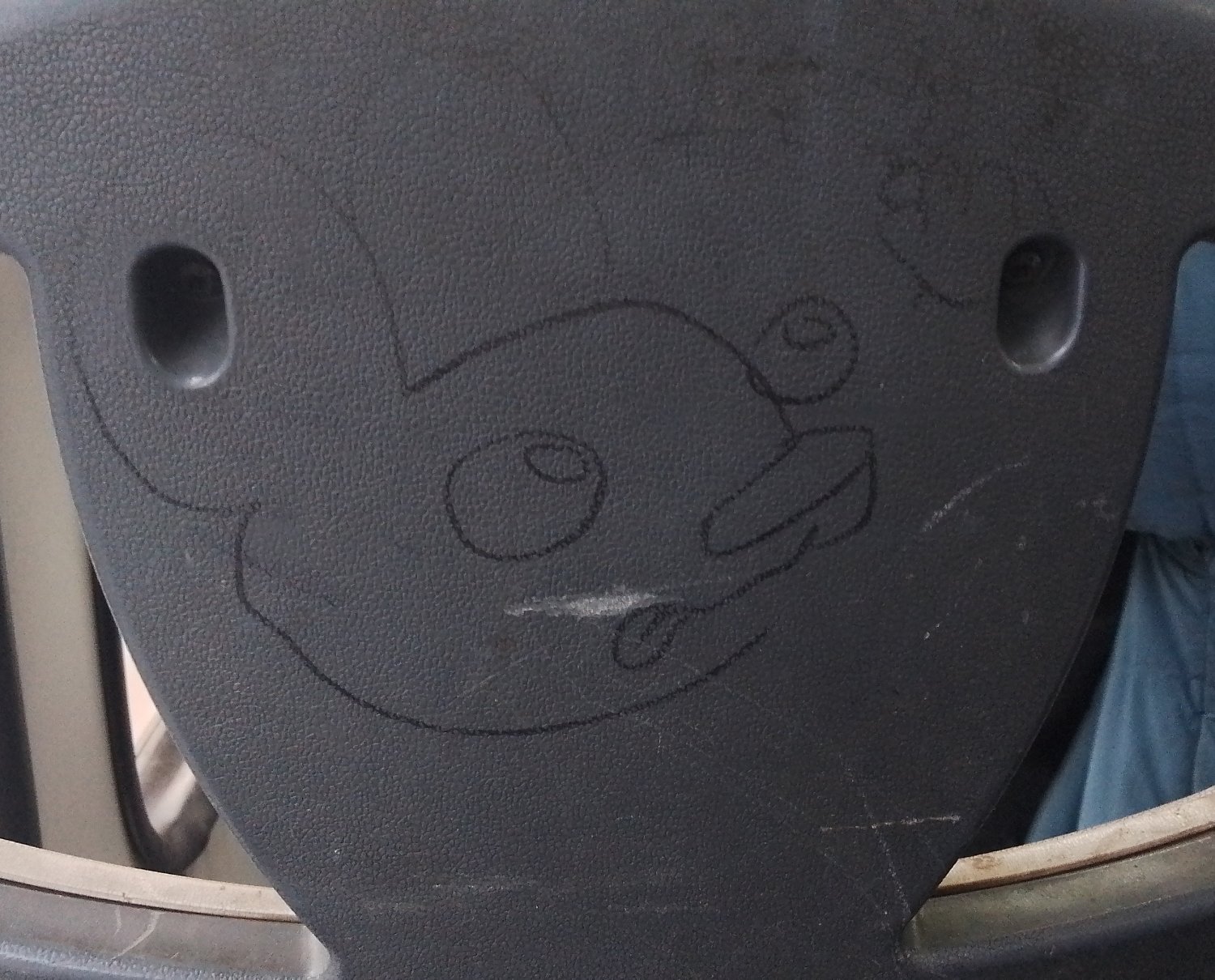 mono en la cabecera tracera del asiento de la micro, con la cara medio tonta, lengua afuera y ojos saltones, con perfil en tres cuartos mirando hacia arriba y levantando la mano